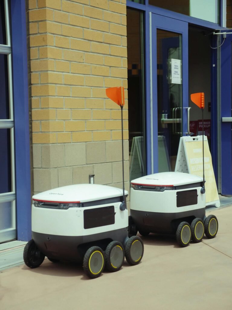 Two modern delivery robots wait outside a building, showcasing advances in technology.